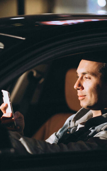 Hombre usando teléfono en coche con tecnología de rastreo y control de riesgos.