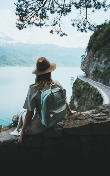 Mujer con mochila observando paisaje y carretera en montaña.